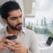 Homme pensif avec café sur balcon urbain